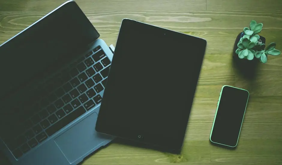 A top-down view of a workspace featuring a laptop, tablet, smartphone, and a small plant.