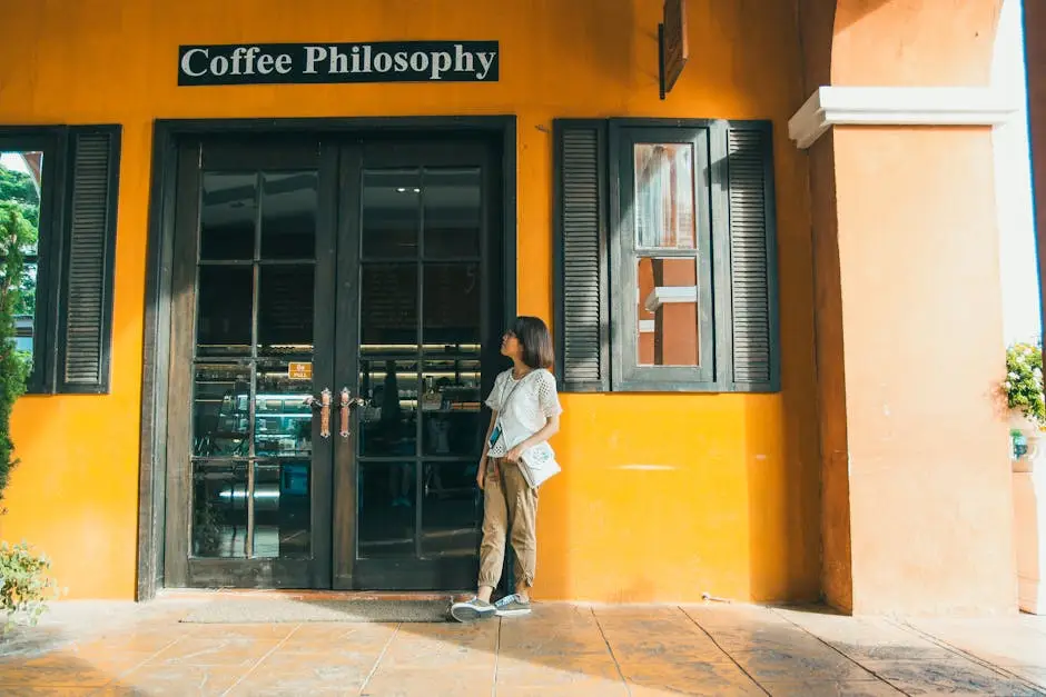 A woman stands outside a vibrant orange coffee shop with a welcoming glass door and sign.
