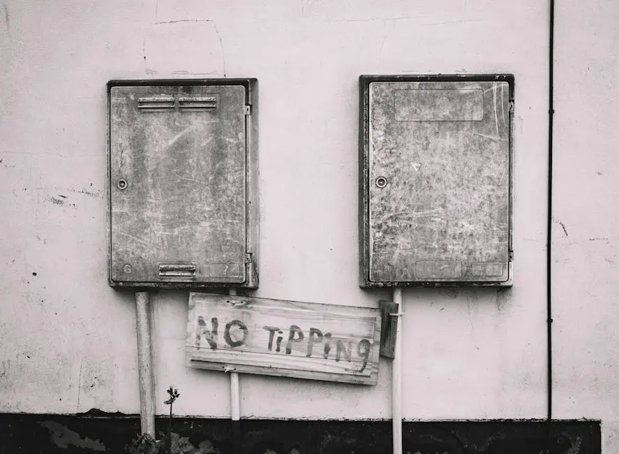 Black and white image of rusty electrical boxes with 'No Tipping' sign adds urban decay aesthetic.